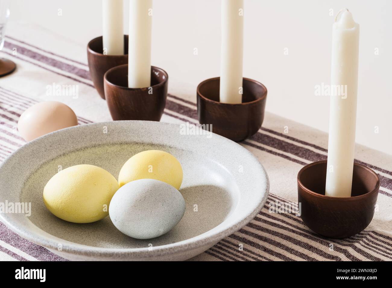 Easter place setting with candles and multi colored eggs, linen tablecloth Stock Photo