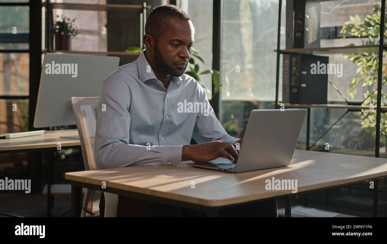 Focused on computer work adult businessman African American senior 40s man worker employer manager specialist programmer typing on laptop at office Stock Photo