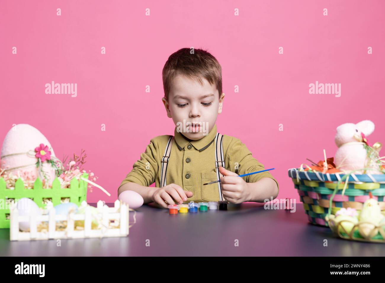 Joyful small child decorating eggs and ornaments with watercolor, coloring and crafting decorations in time for easter sunday celebration. Young cheerful boy painting with tie dye. Stock Photo