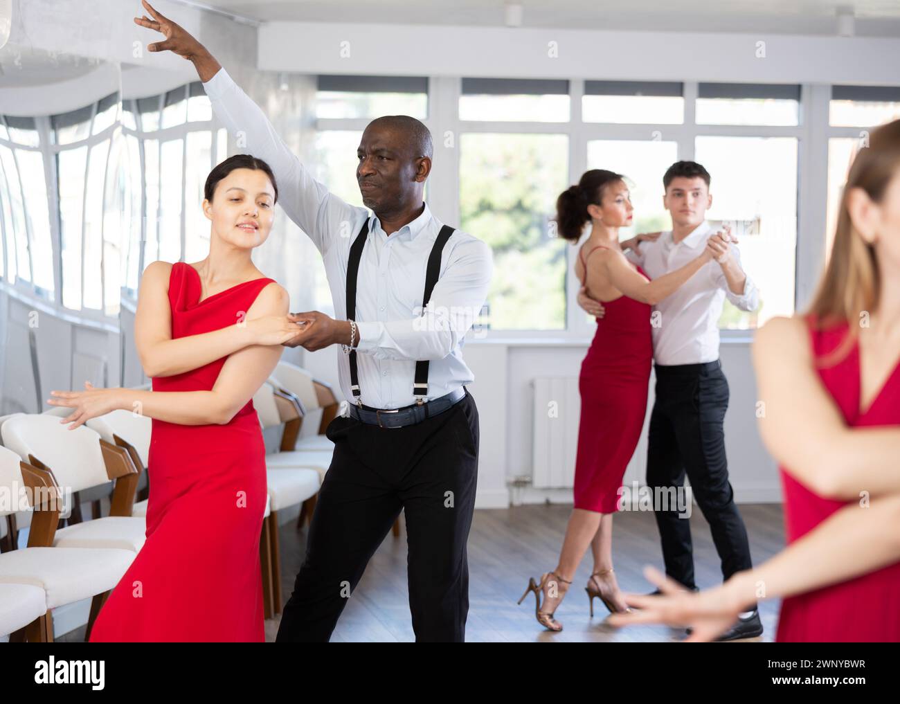 Smiling young woman and African american partner successfully perform mesmerizing movements of paso doble dance during party Stock Photo
