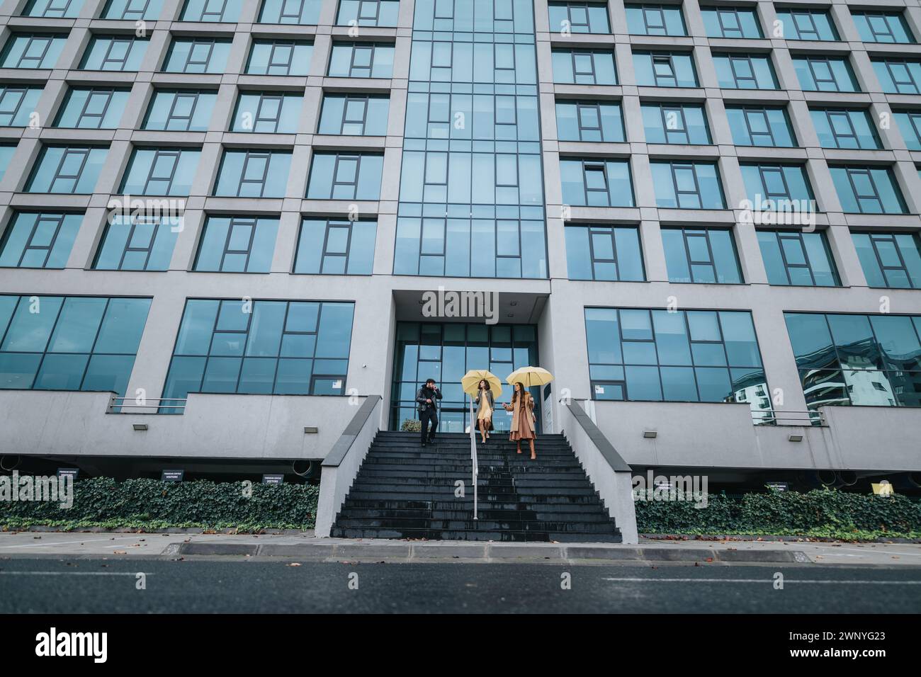 Two professional women carrying yellow umbrellas descend the steps of a ...
