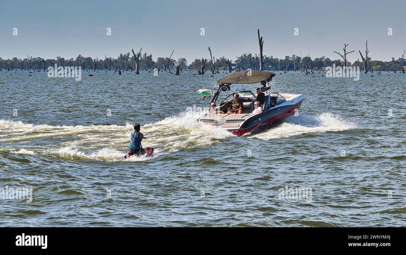 Yarrawonga, Victoria, Australia - 17 April 2022: Thrilling wakeboarding session on Lake Mulwala's choppy waters with dead trees in the background Stock Photo