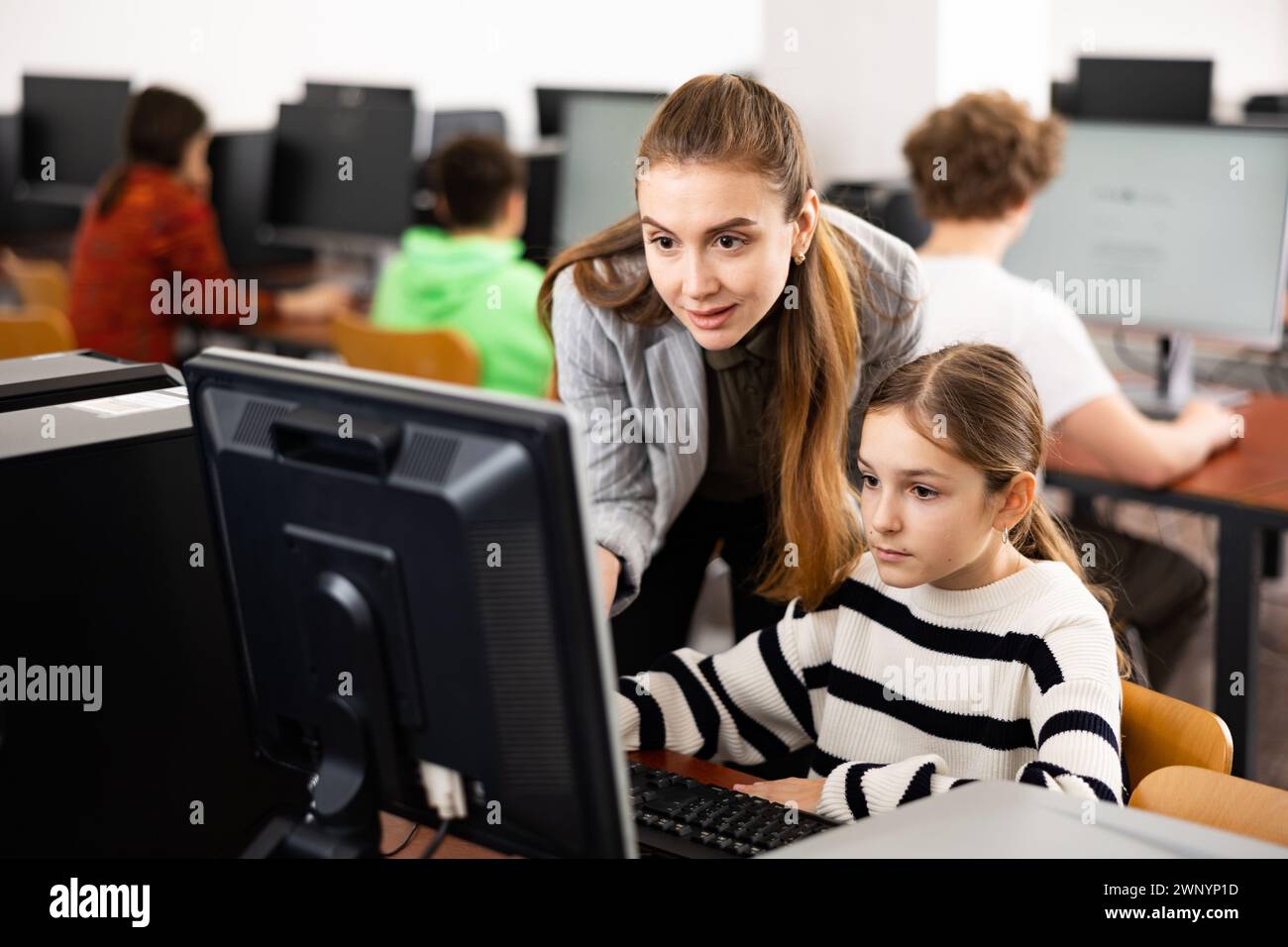 Female teacher talking to focused teen girl student in computer class ...