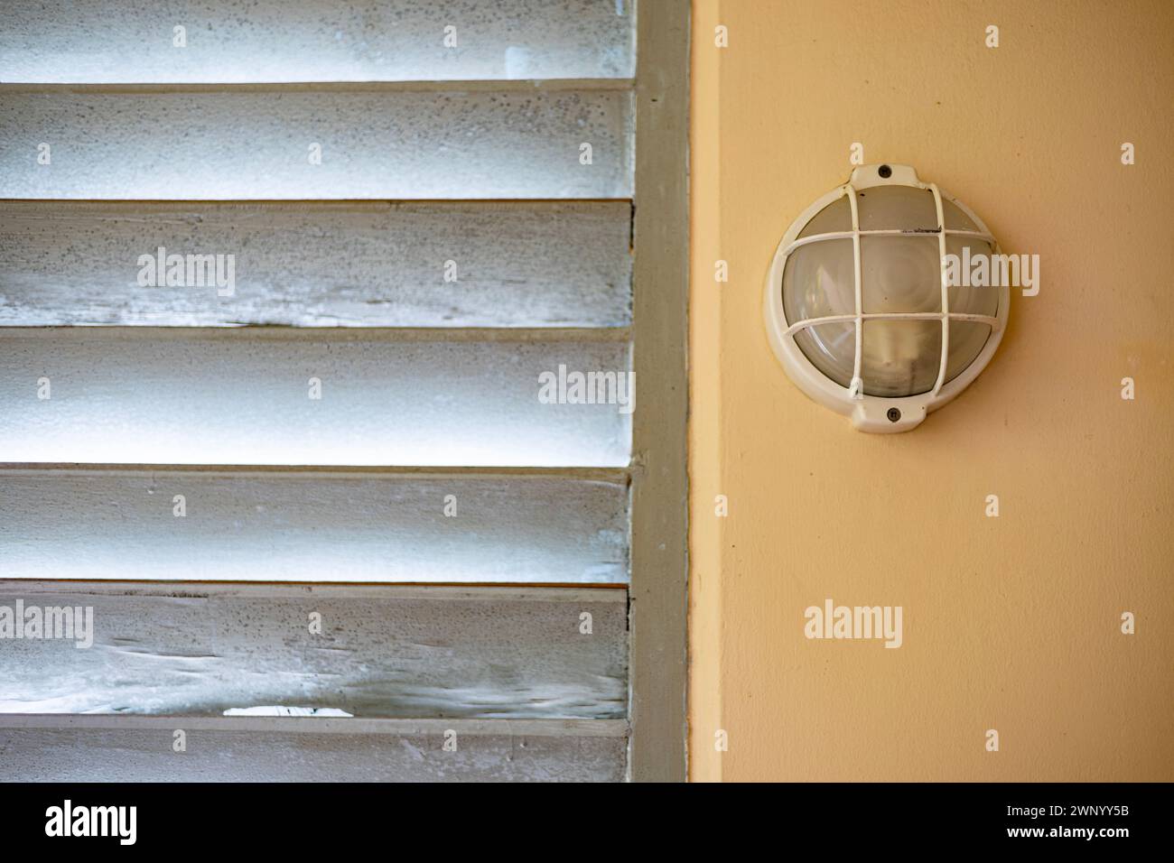 Old circle wall lamp in the right of louver window. Vintage wall. Stock Photo