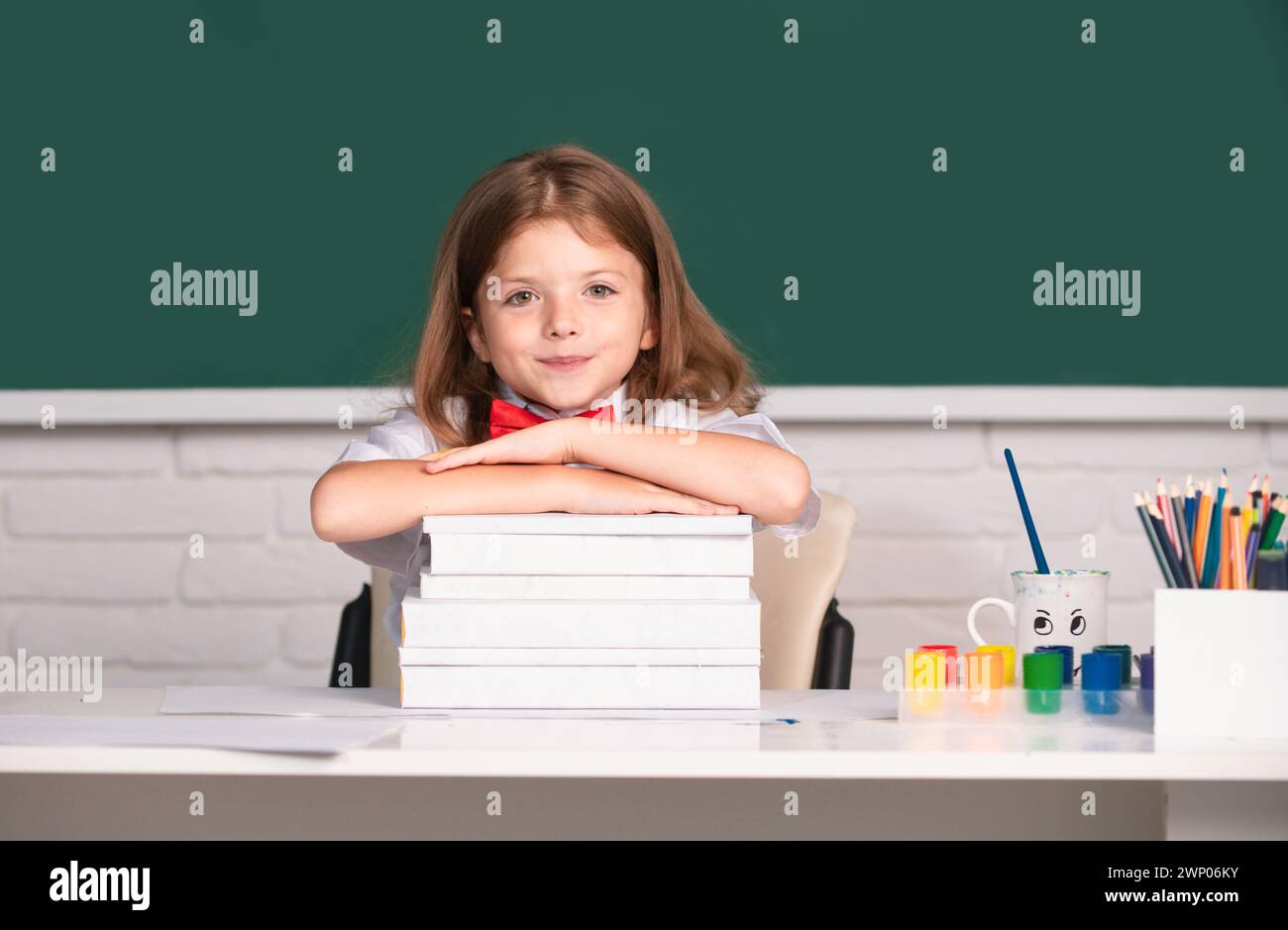 Smiling girl sitting at the desk and holding hands on the books in the ...