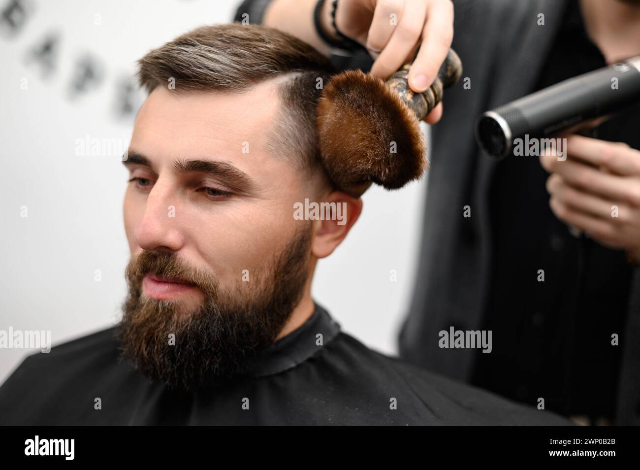 The hairdresser sweeps the hair during the haircut with a brush and cold drying air. Stock Photo