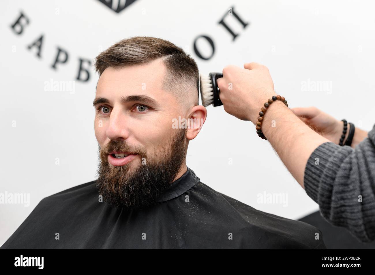 Barber sweeps hair with a brush while cutting a clients hair in a salon. Stock Photo