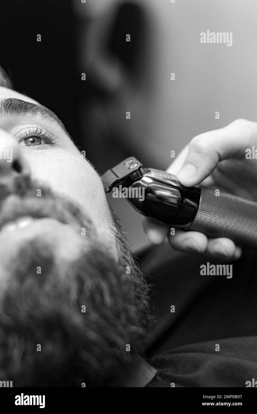 Cutting a gentleman beard in a barbershop with a clipper. Shortening the length of the beard from the sides by the master for the client. Stock Photo