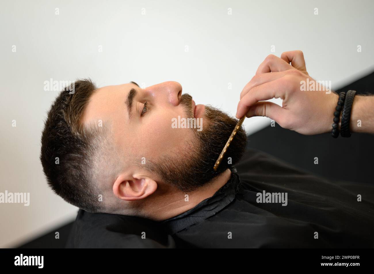 Barber combs beard with comb while cutting and shaving Caucasian man Stock Photo