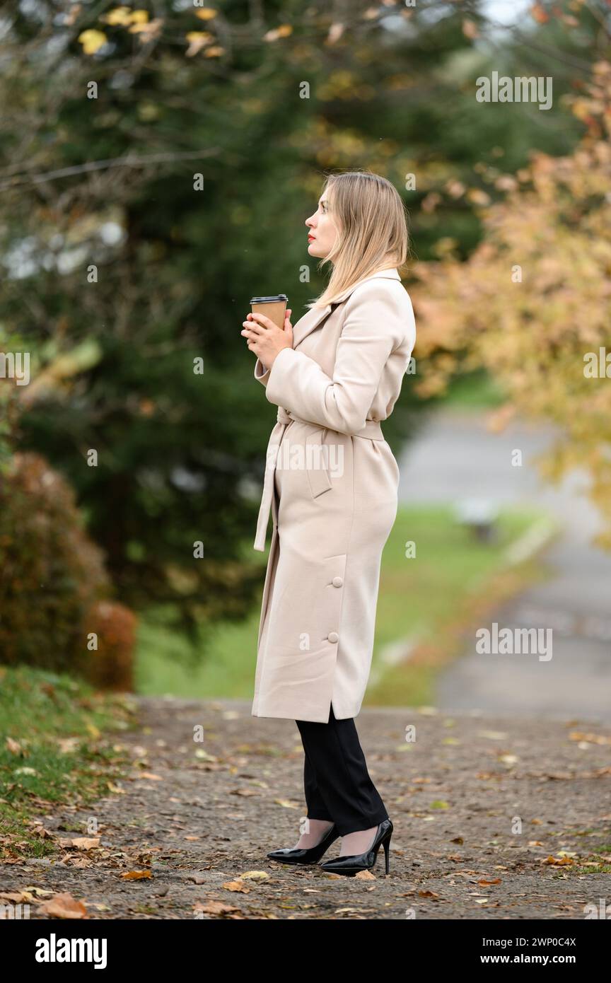 A young girl in the autumn park drinks coffee, rest in the park. Stock Photo