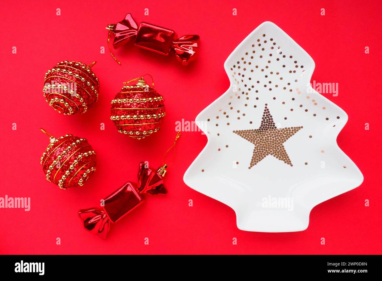 Christmas tree with gold ornaments and a star in the middle. Red background. Christmas decorations and two sweet candies. Three red balls with gold Stock Photo