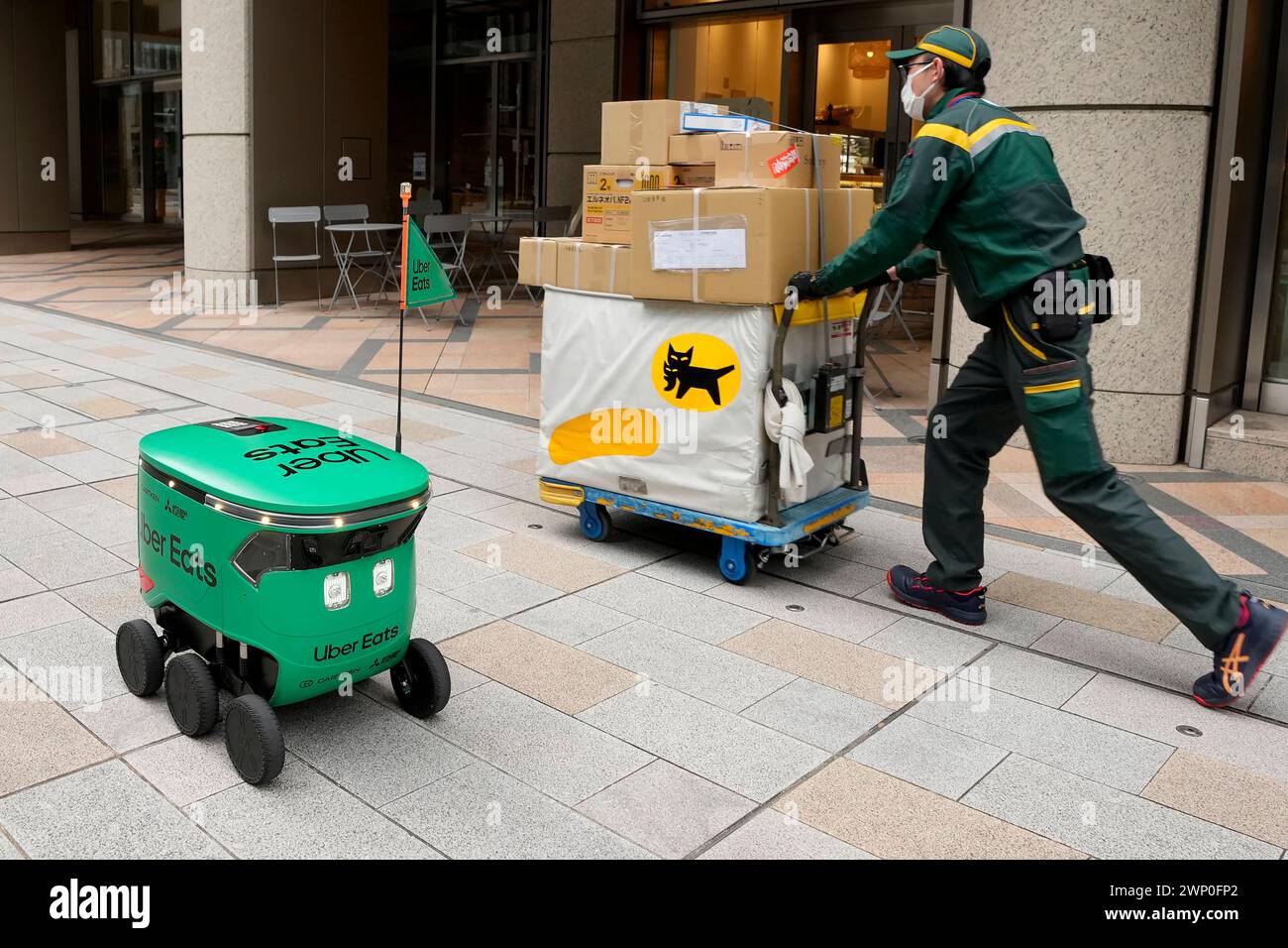 An Uber Eats food delivery robot walks past a delivery person during ...