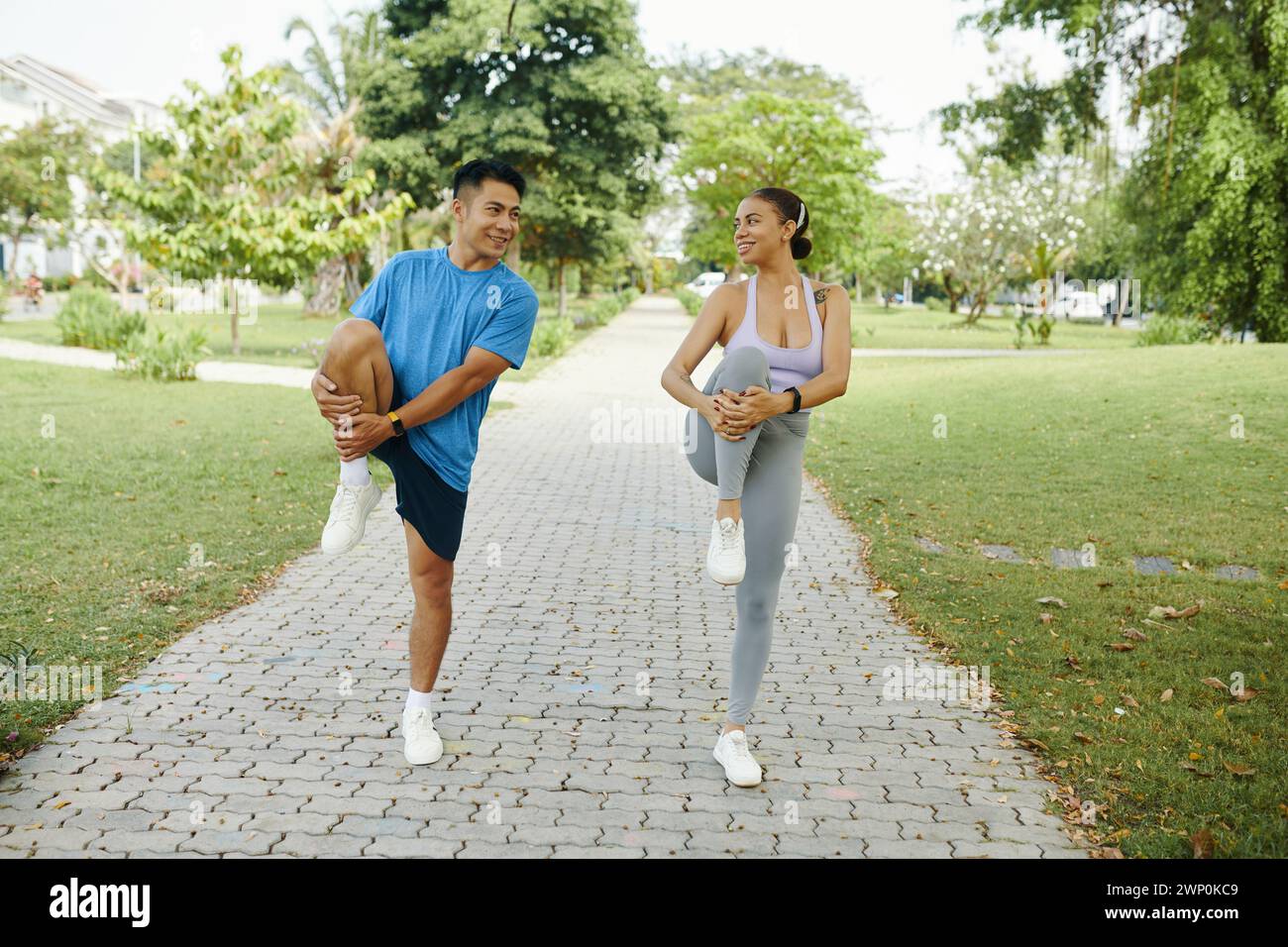 Happy diverse couple doing leg stretch exercise before morning run Stock Photo