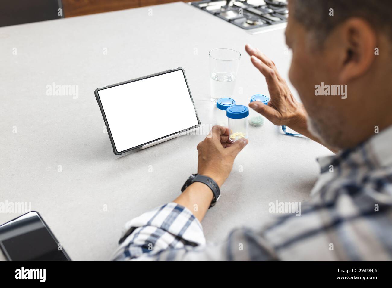 A senior man is examining medication next to a tablet with a blank screen, providing copy space Stock Photo