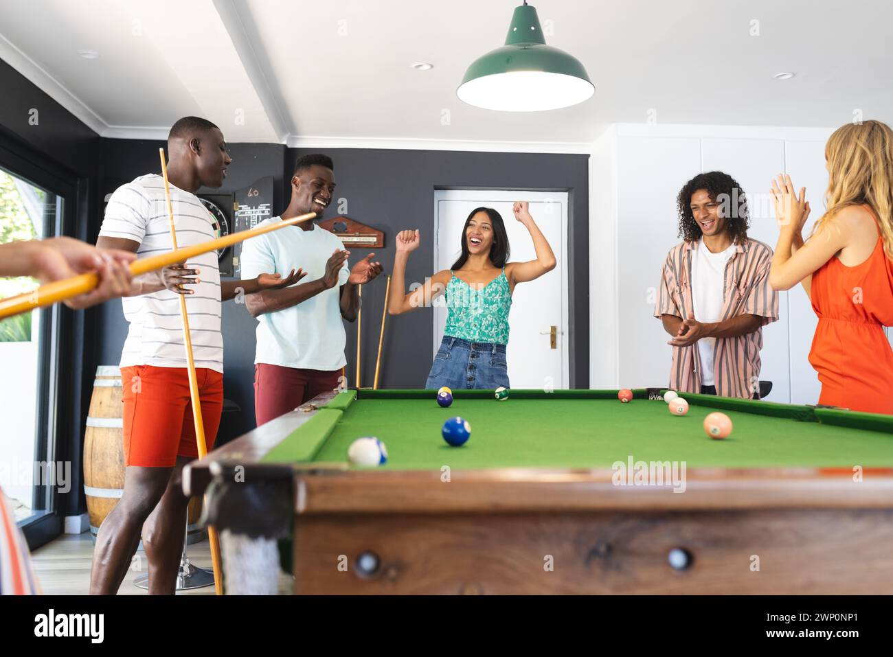 Diverse group of friends enjoys a game of pool in a brightly lit room Stock Photo