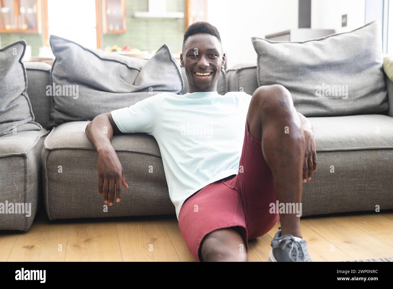 Young African American man with a bright smile sits relaxed on a grey sofa Stock Photo