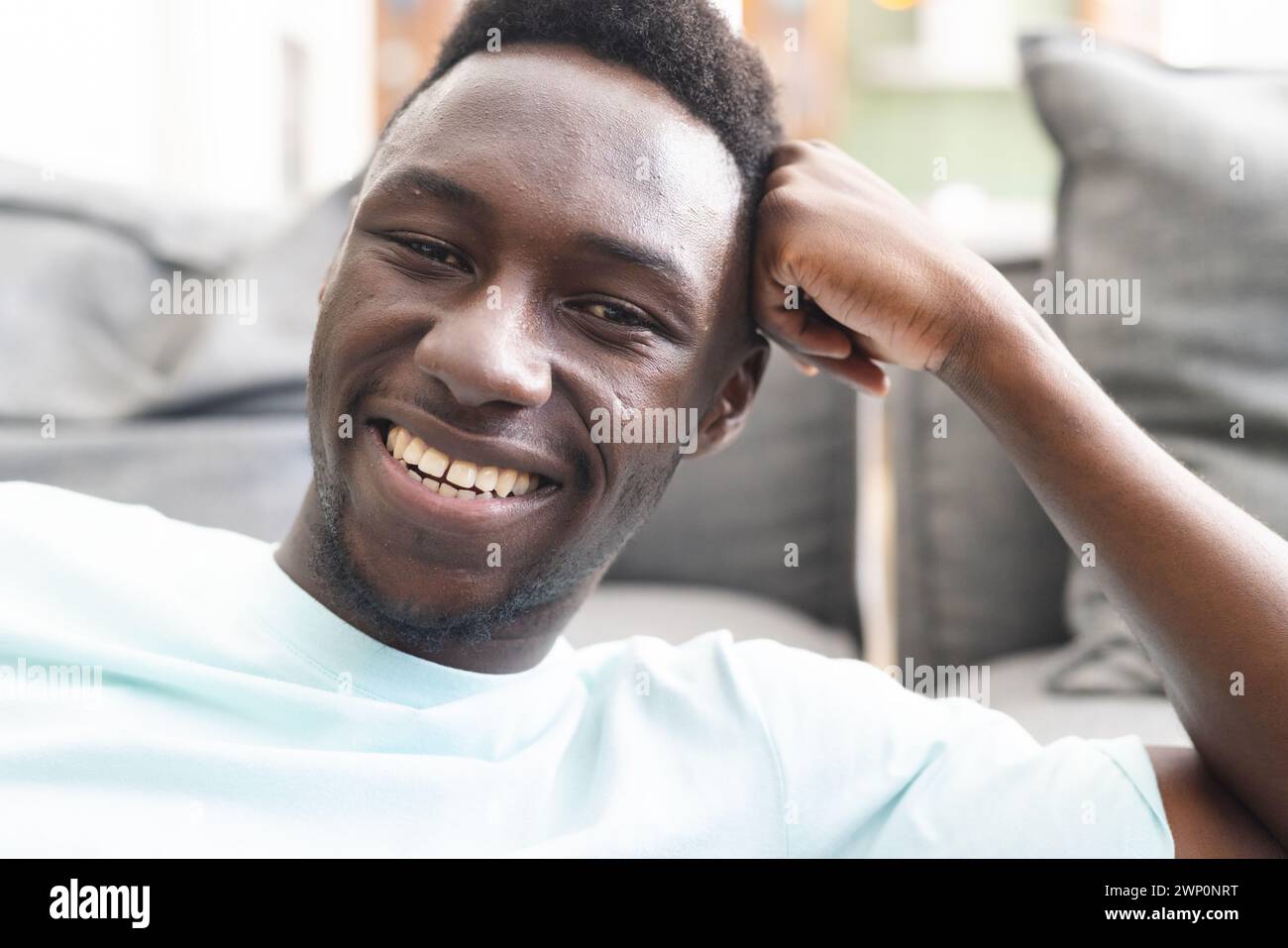 Young African American man smiles broadly, showcasing a casual style in a light blue shirt Stock Photo