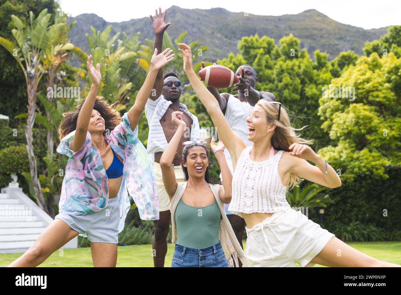 Diverse group of friends playing with a football outdoors, expressions of joy evident Stock Photo