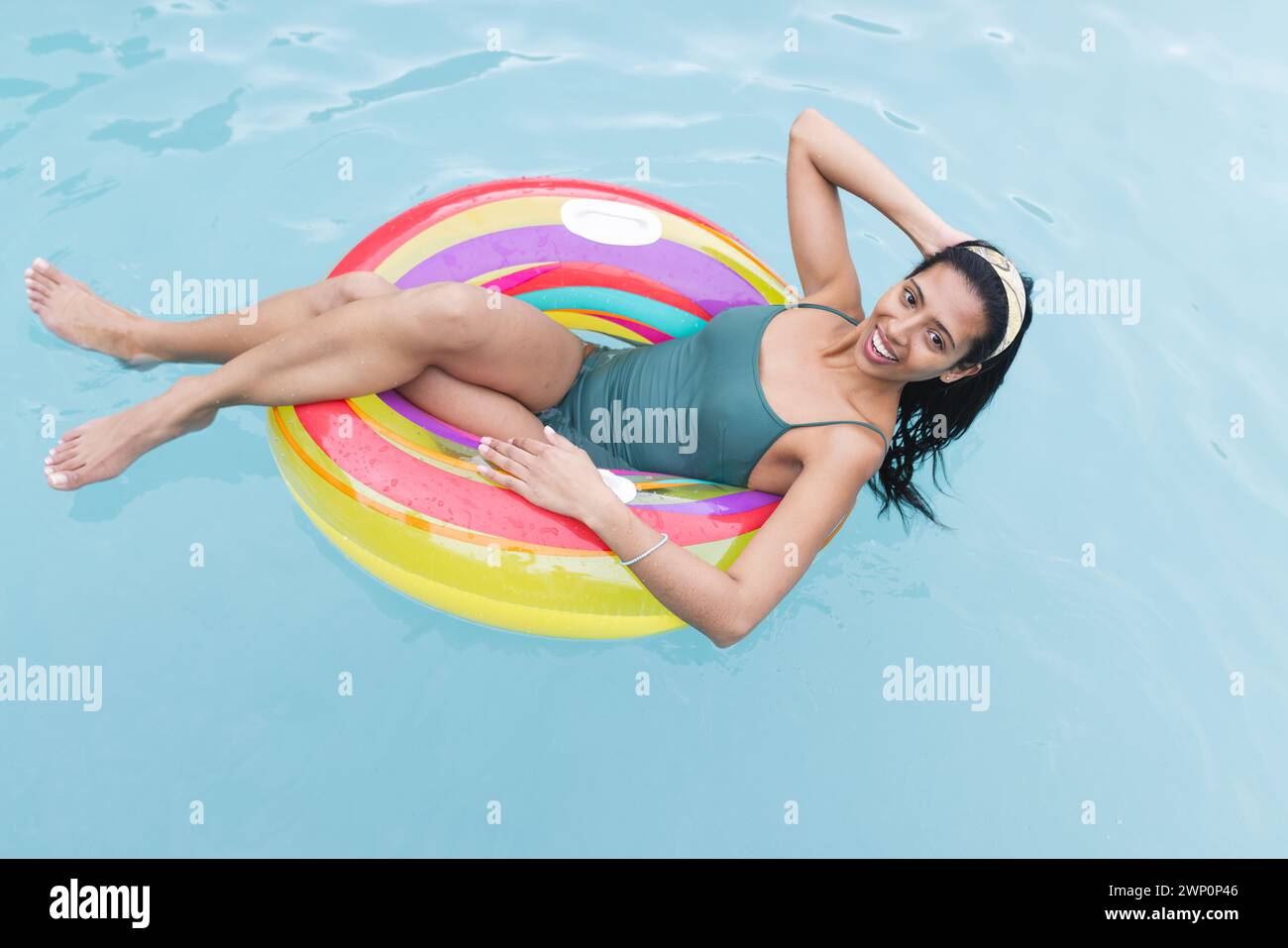 Young biracial woman lounges on a colorful pool float, her dark hair tied back Stock Photo