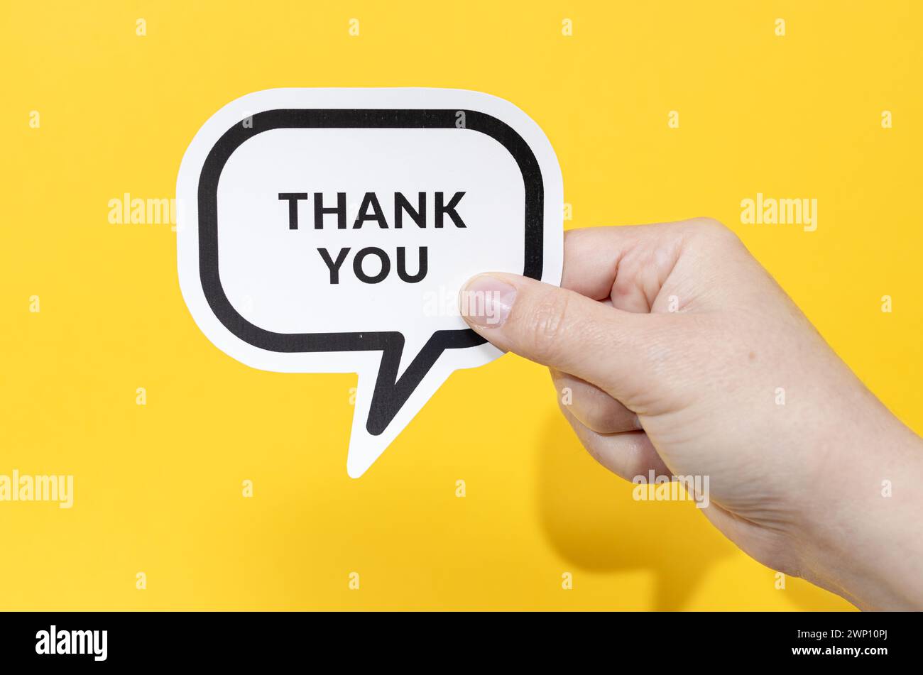Hand holding speech bubble with Thank You text isolated on yellow background Stock Photo