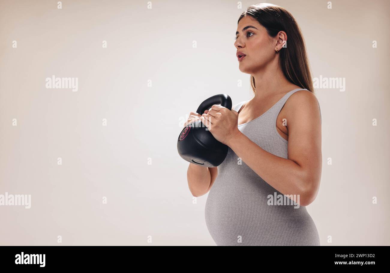 Pregnant woman exercises in a studio, lifting weights and focusing on