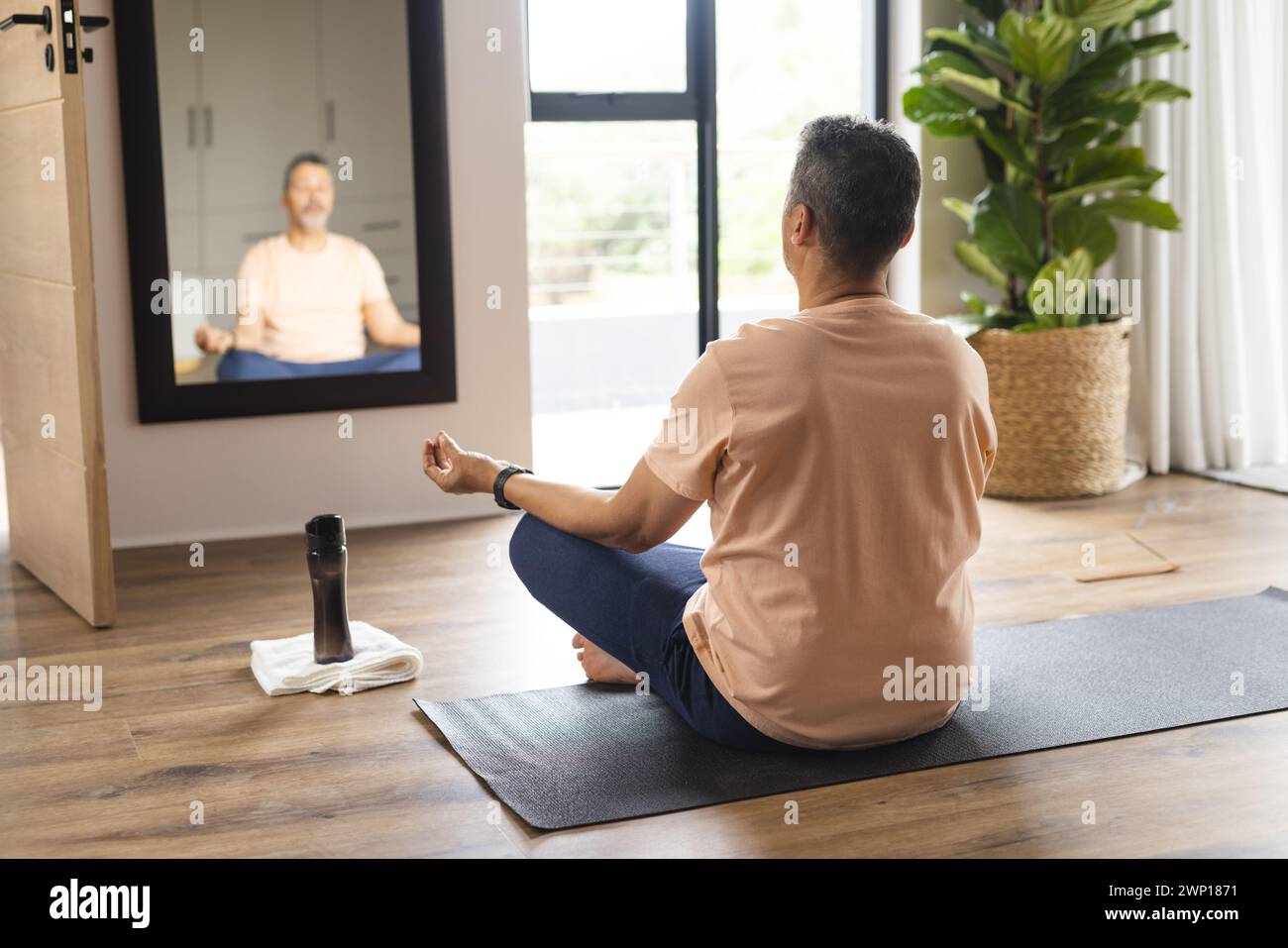 Biracial senior man meditates in front of a mirror, reflecting a peaceful posture Stock Photo