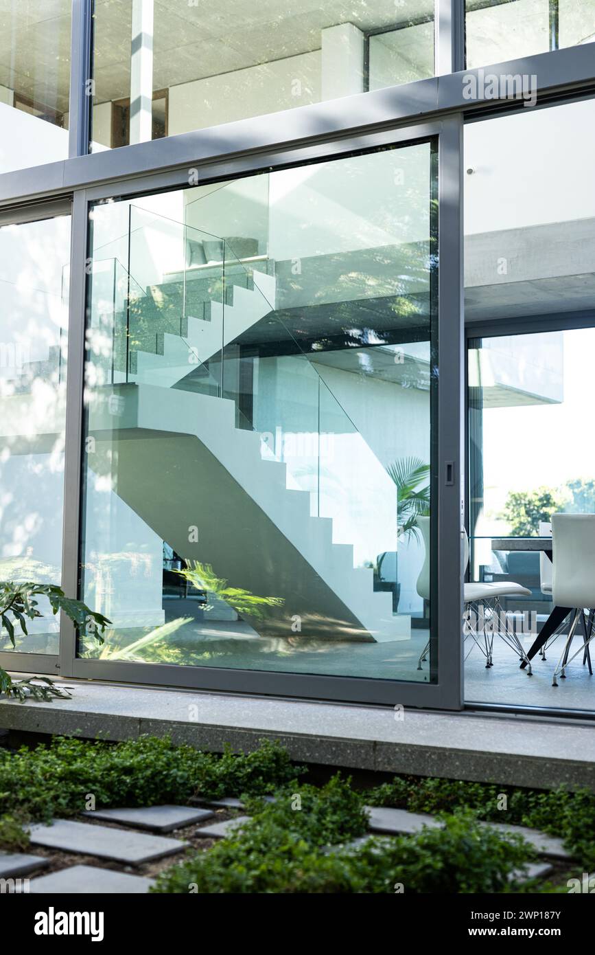 A modern staircase is visible through the large glass window of a contemporary house Stock Photo