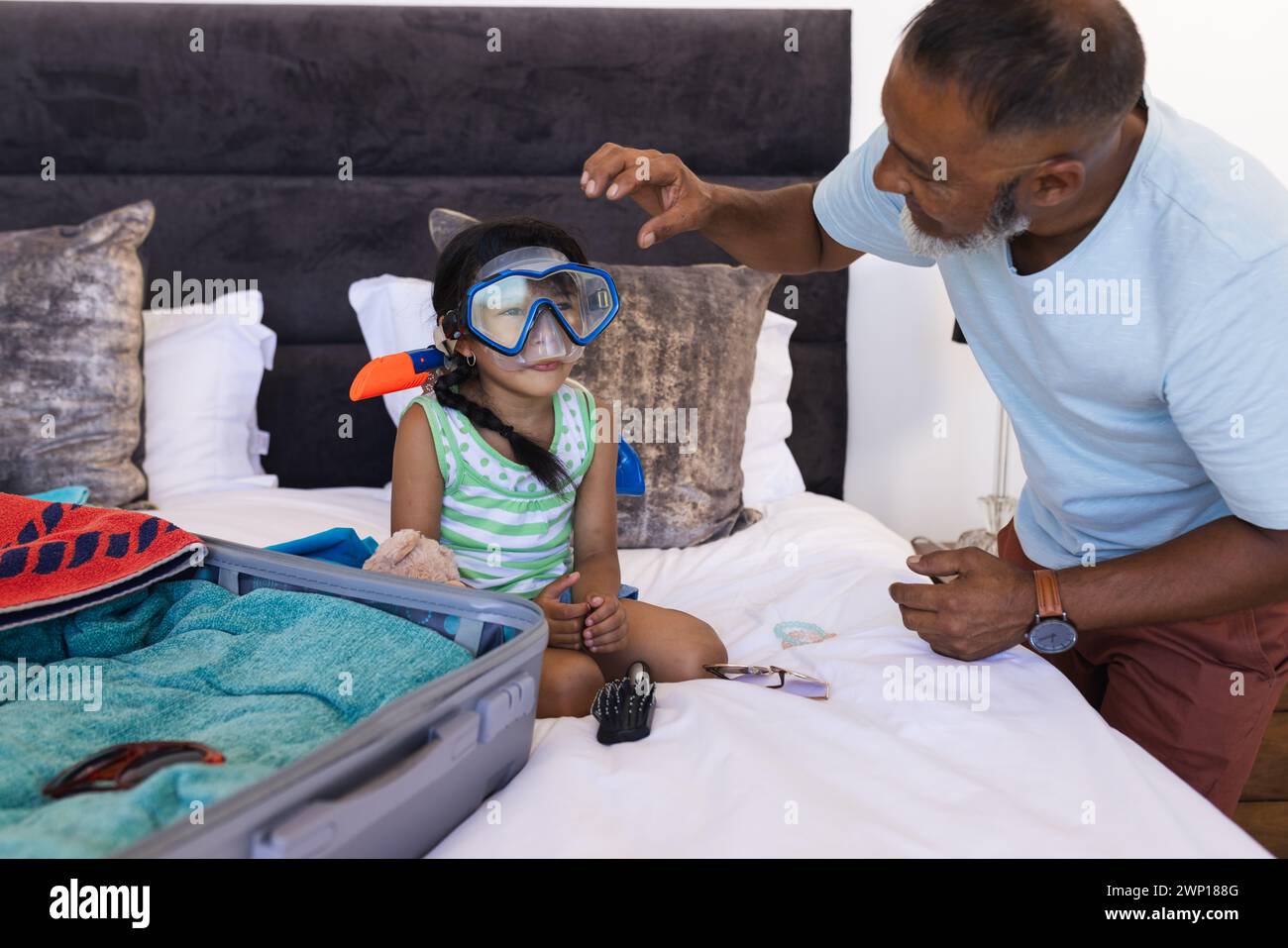 Grandfather helps his young granddaughter try on snorkeling gear in a bedroom Stock Photo
