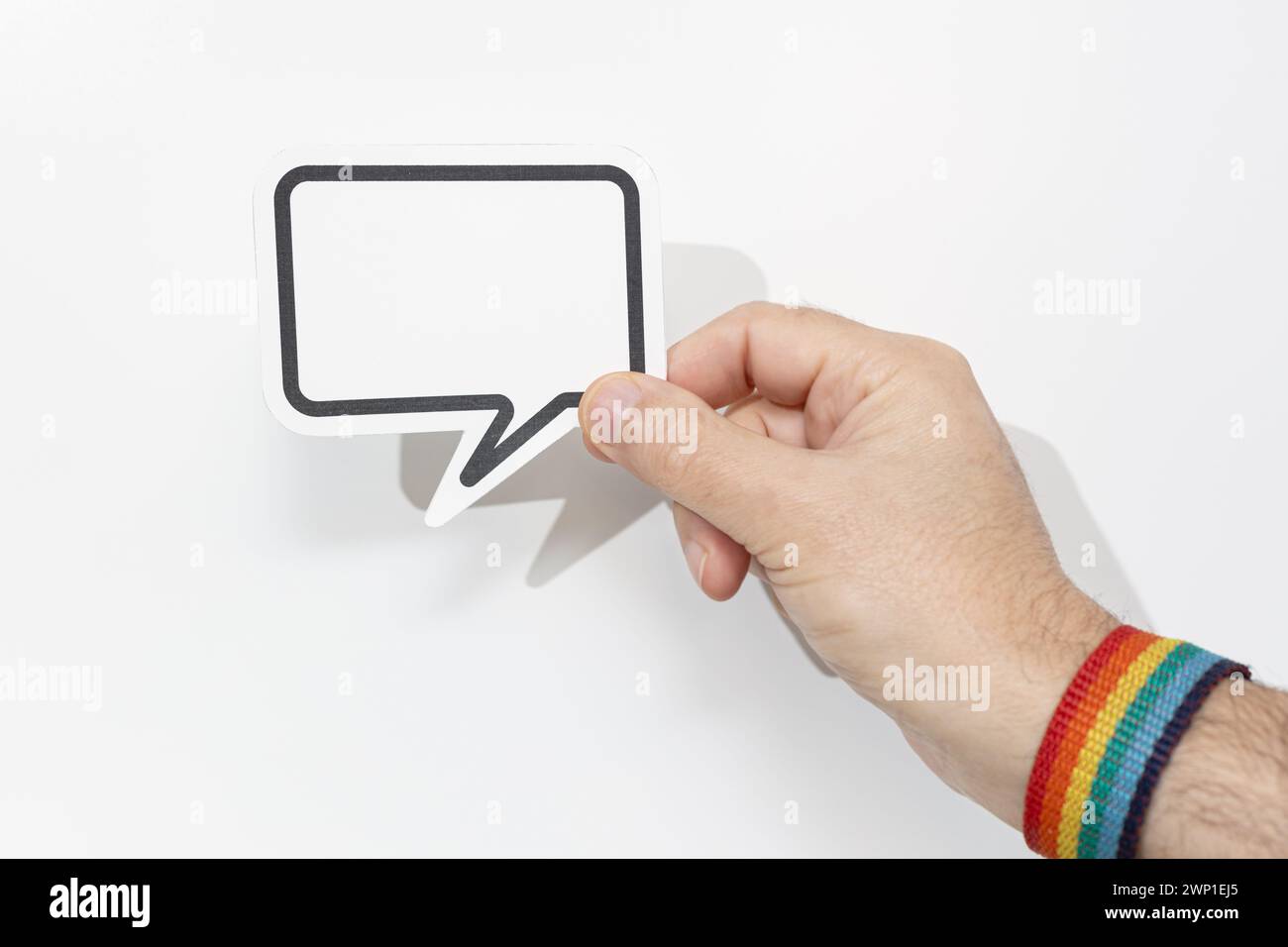 Hand wearing pride flag bracelet holding blank speech bubble on white background. Template Mockup Stock Photo