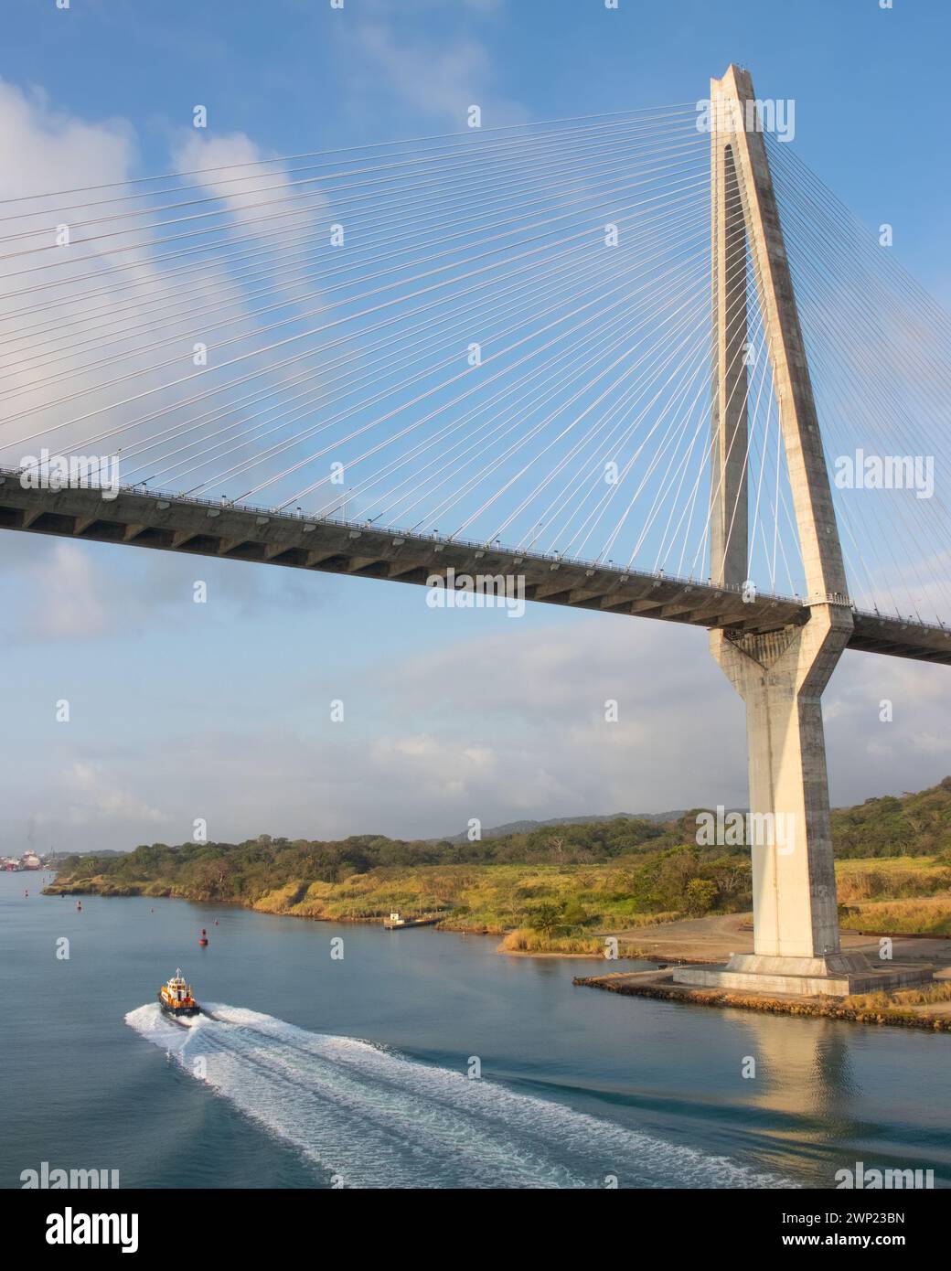 Small boat passed underneath the large impressive Atlantic Bridge at Colon Panama at start of the Panama Canal set against blue sky low water levels Stock Photo