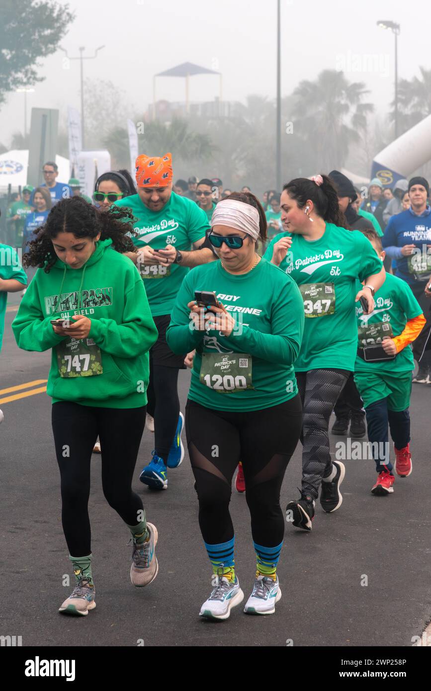 Group of walkers in green t-shirts, some on their cell phones, on a foggy day in St. Patrick’s Day 5K Run & Walk Pharr, Texas, USA. Stock Photo