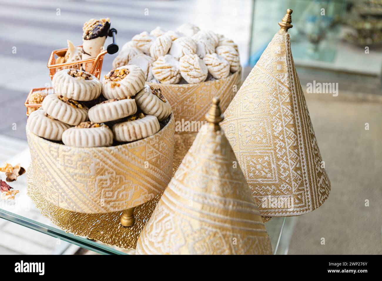 Horizontal photo a visually engaging assortment of Arabic sweets on golden stands, with ornate geometric fabric covers adding cultural richness. Food Stock Photo