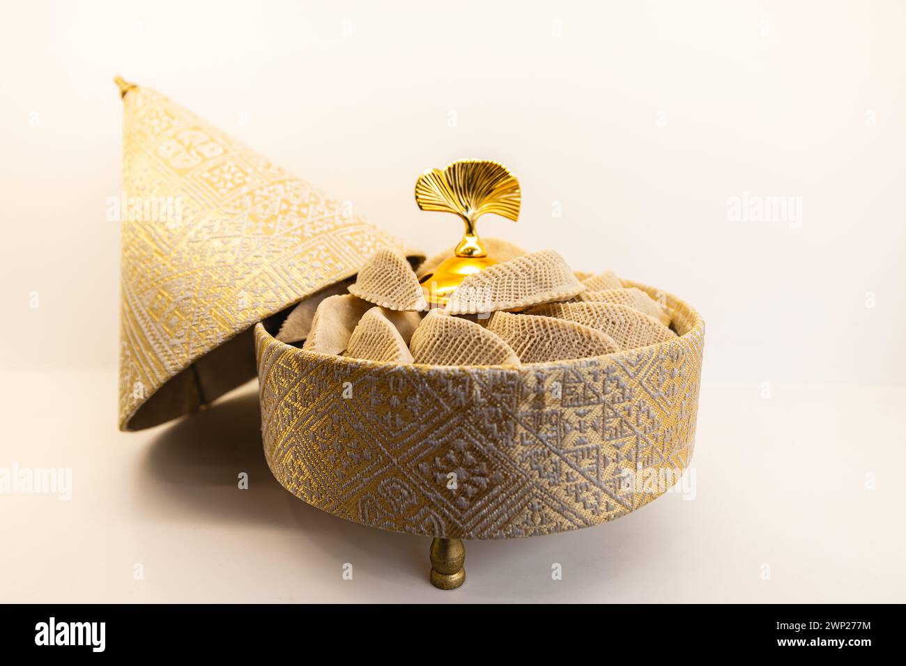 Horizontal photo a golden, embroidered container, ornately designed with a geometric pattern, holds a selection of traditional Arabic pastries against Stock Photo