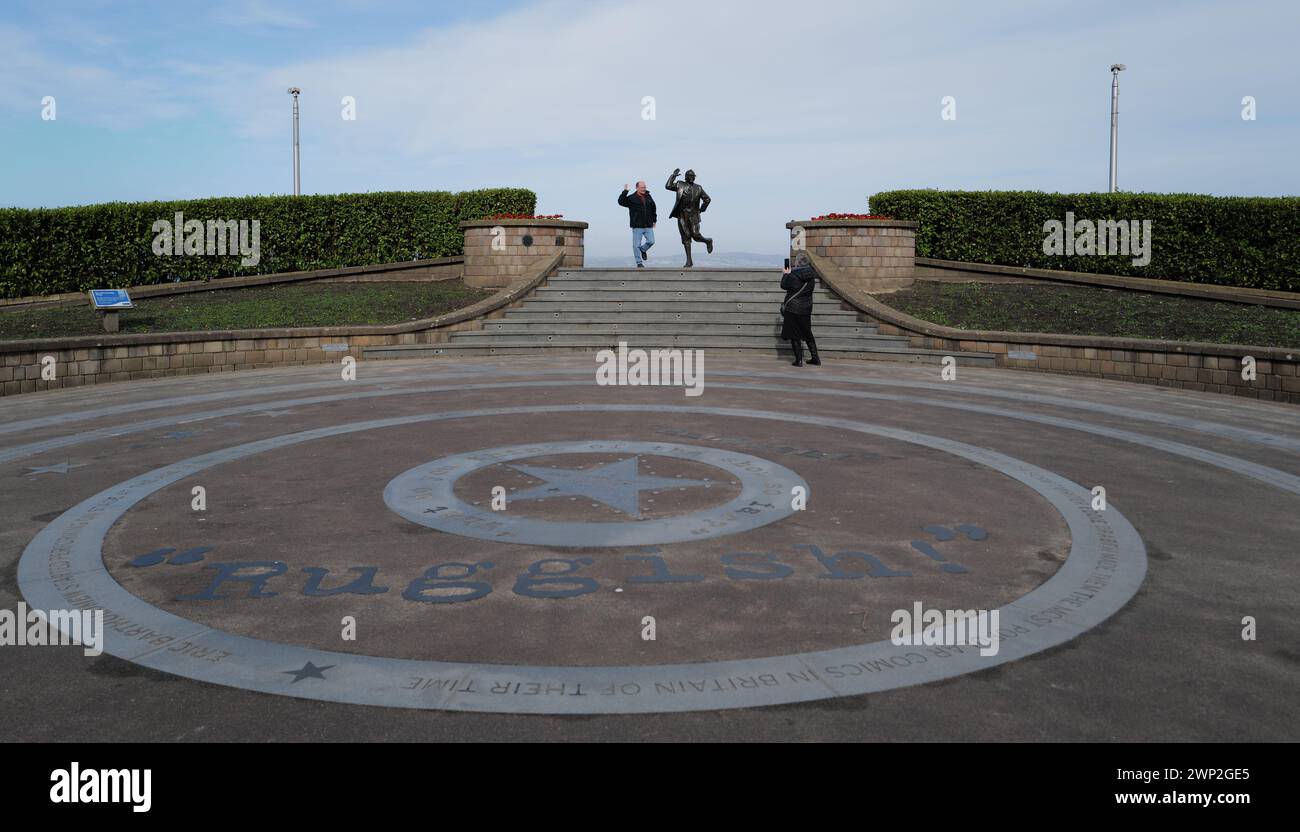 A pan poses for a photograph alongside Eric Morecambe’s statue in Morecambe, Lancashire. Unveiled by the Queen in 1999, the slightly larger than life-sized statue depicts Eric Morecambe in one of his characteristic poses with a pair of binoculars around his neck (he was a keen ornithologist). The statue is set against the stunning backdrop of Morecambe Bay and the Lake District hills Stock Photo