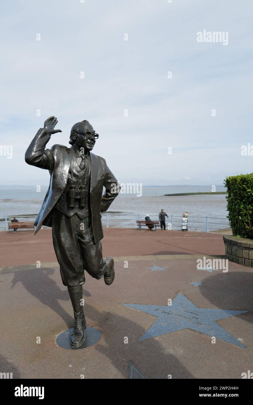 Eric Morecambe statue overlooking the sea in Morecambe, Lancashire. Unveiled by the Queen in 1999, the slightly larger than life-sized statue depicts Eric Morecambe in one of his characteristic poses with a pair of binoculars around his neck (he was a keen ornithologist). The statue is set against the stunning backdrop of Morecambe Bay and the Lake District hills Stock Photo