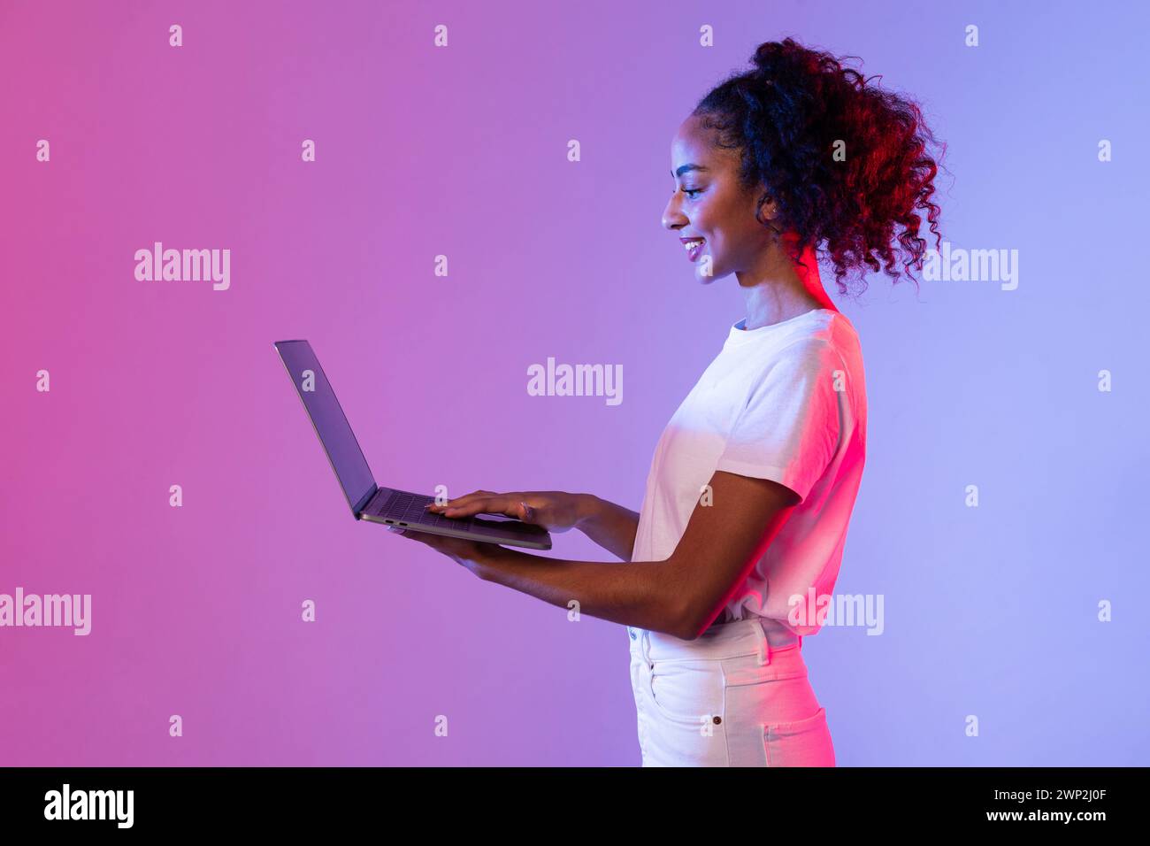 Smiling black woman using laptop with neon light background Stock Photo