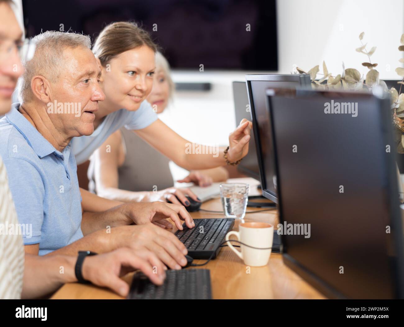 Young female mentor explaining something to elderly man during computer class Stock Photo