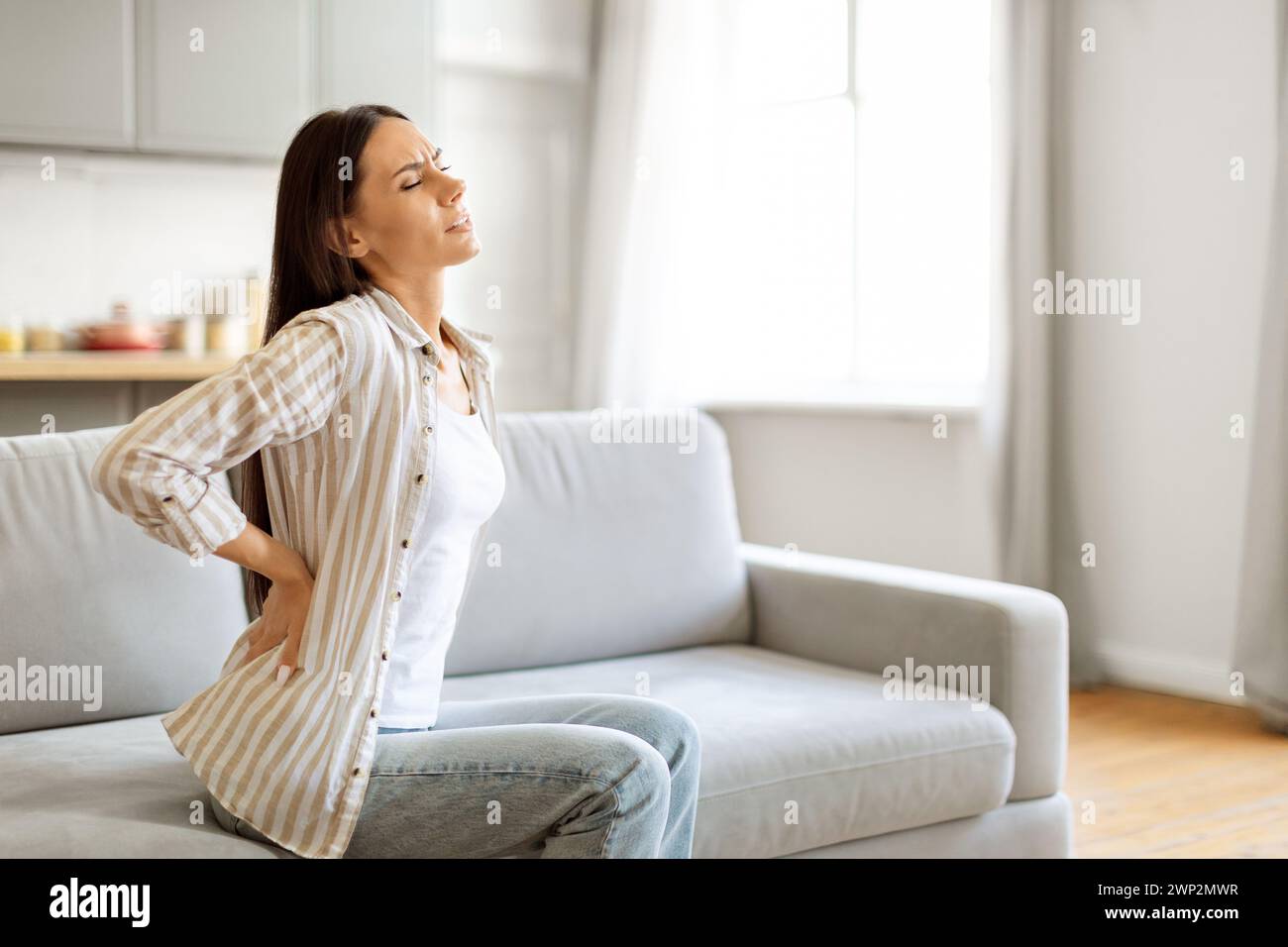 Backache. Young Woman Massaging Aching Back While Sitting On Couch At ...
