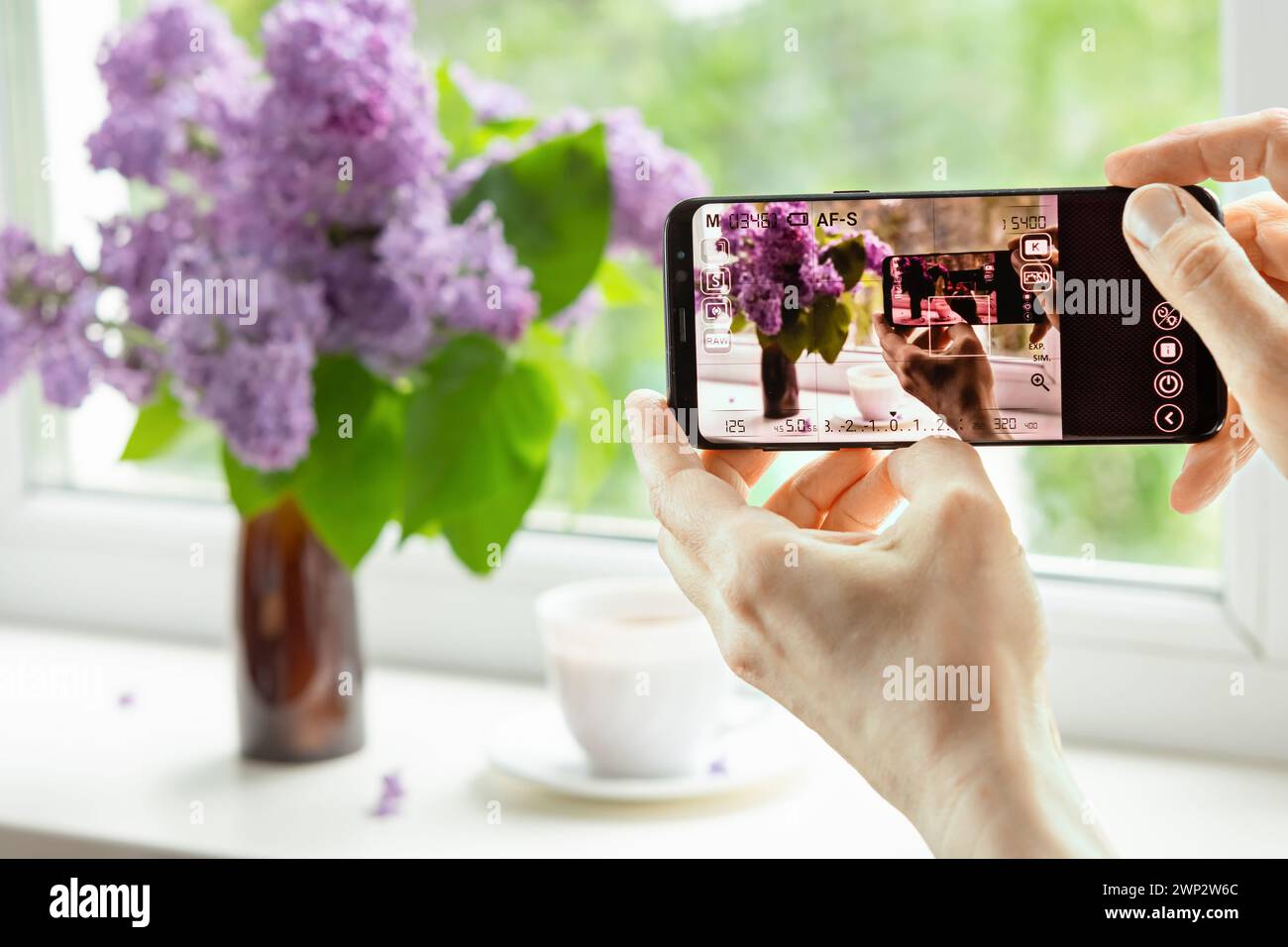 woman photographs a lilac flower arrangement at home with a camera remotely via an application on a smartphone. Remote camera control technology Stock Photo