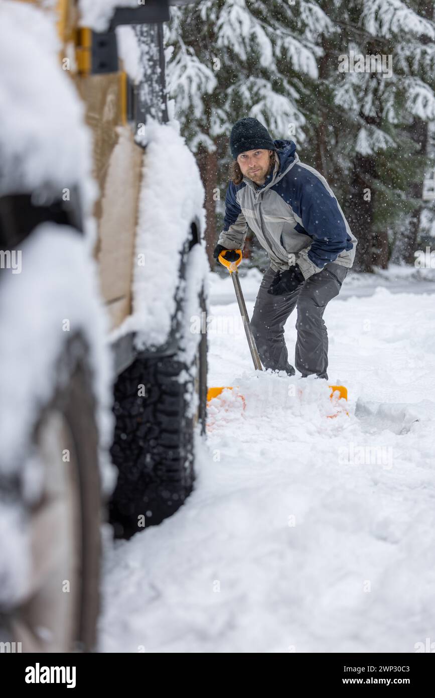 A man is shoveling snow off the road. The snow is piled up on the ground and the man is using a shovel to clear it Stock Photo