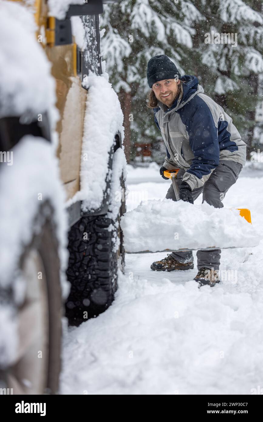 A man in a black hat and blue jacket is shoveling snow off the back of a truck Stock Photo