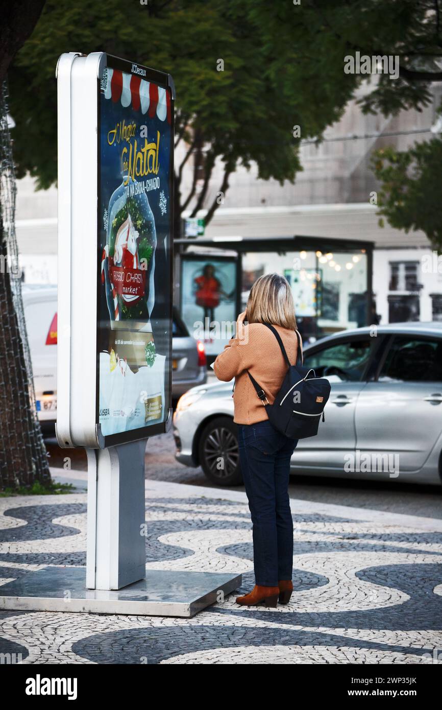 A woman reads advertising information from a billboard, absorbing its message attentively Stock Photo