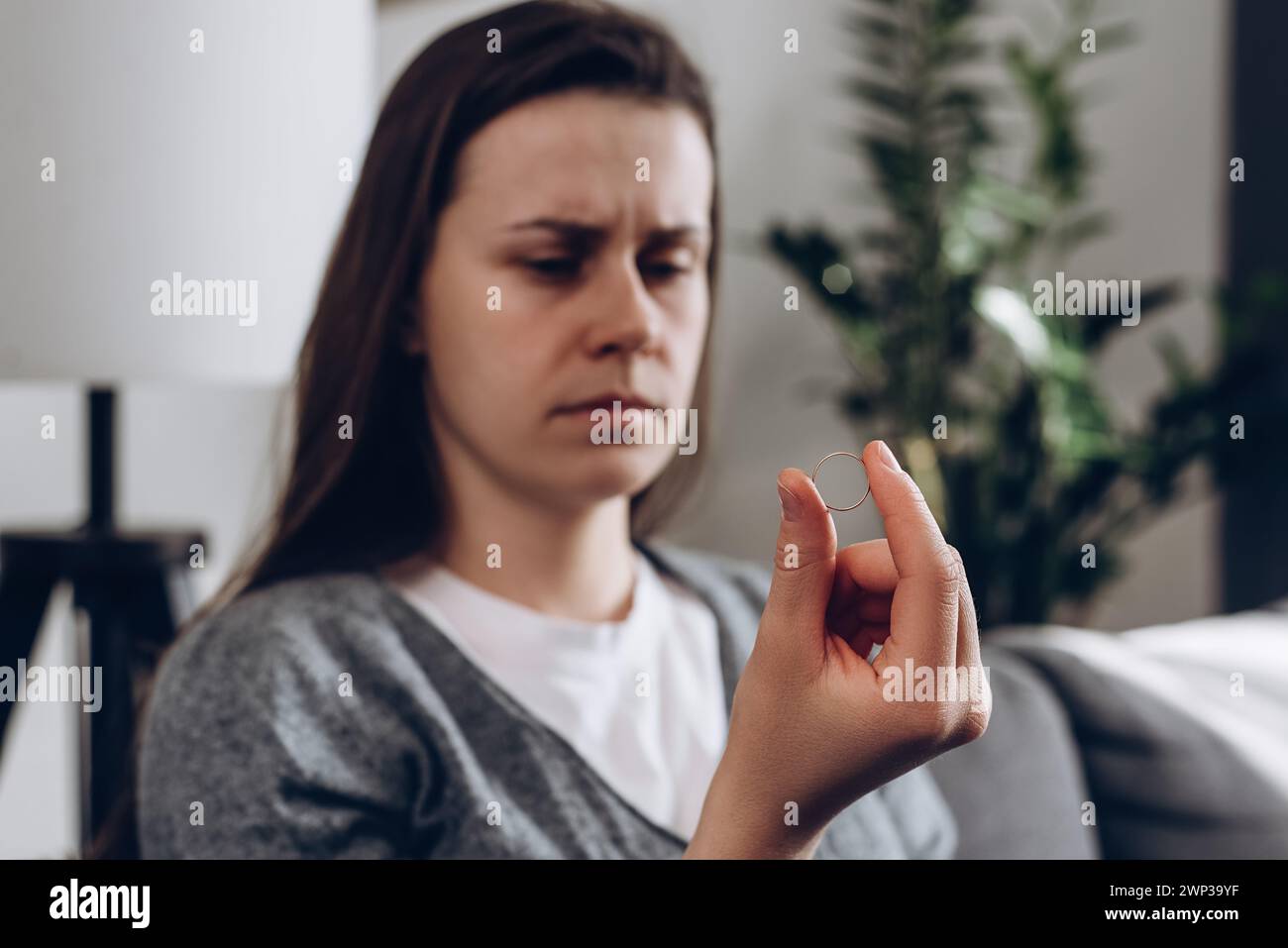 Worried depressed young woman holding wedding ring sitting alone on