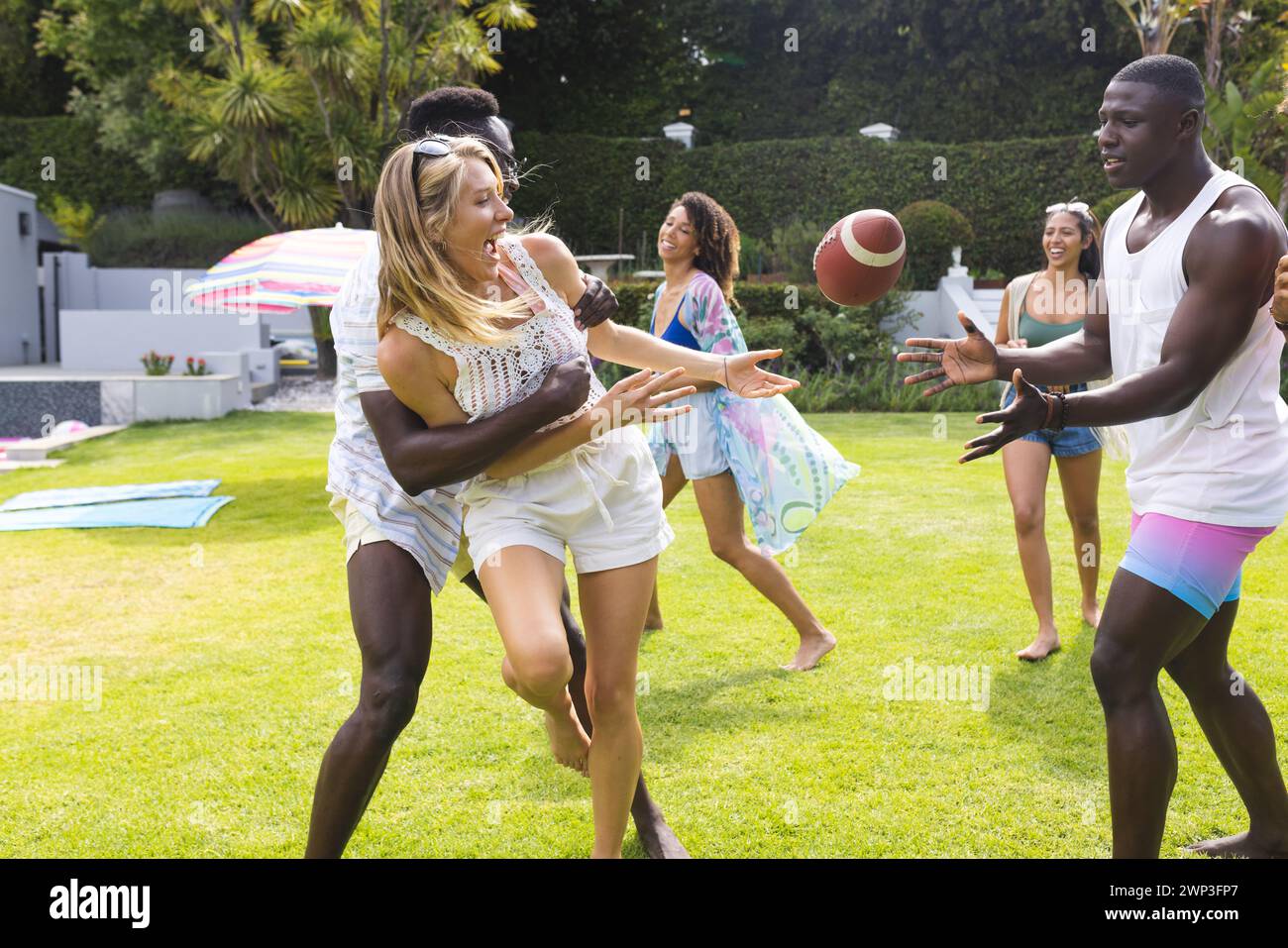 Young Caucasian woman catches a football, cheered on by a young African American man Stock Photo