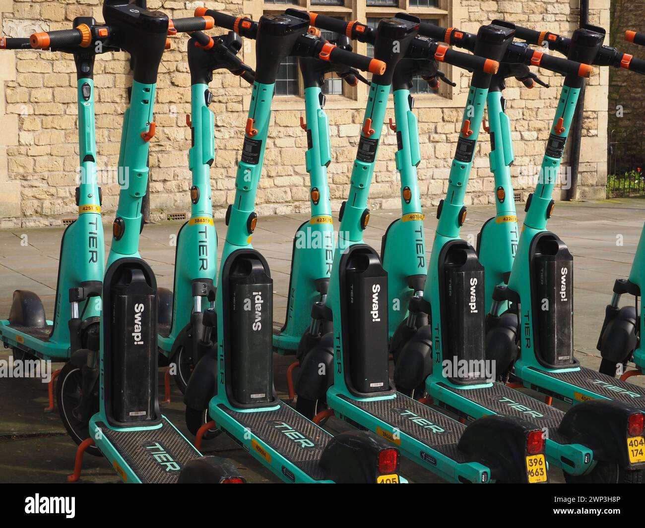 Row of bright green West scoot electric scooters operated by German company Tier in James Street West, Bath, Somerset. Stock Photo