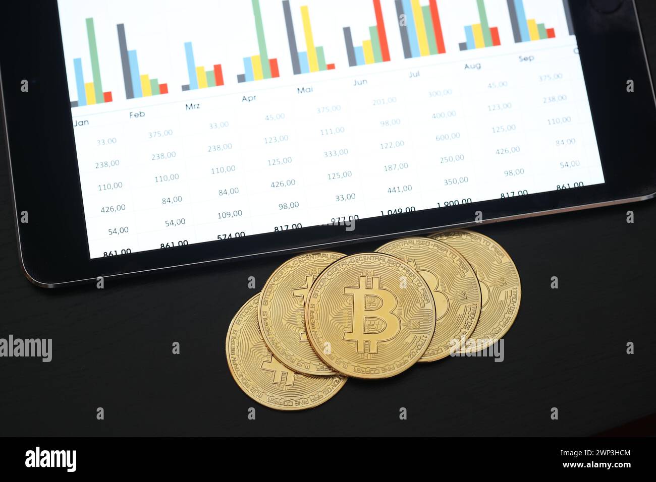 Symbolbild:  Bitcoins vor einem Tablet mit Finanzdaten - Der Bitcoin steht hoch im Kurs. Selbst Finanzdienstleister wie Paypal wollen die Kryptowährun Stock Photo