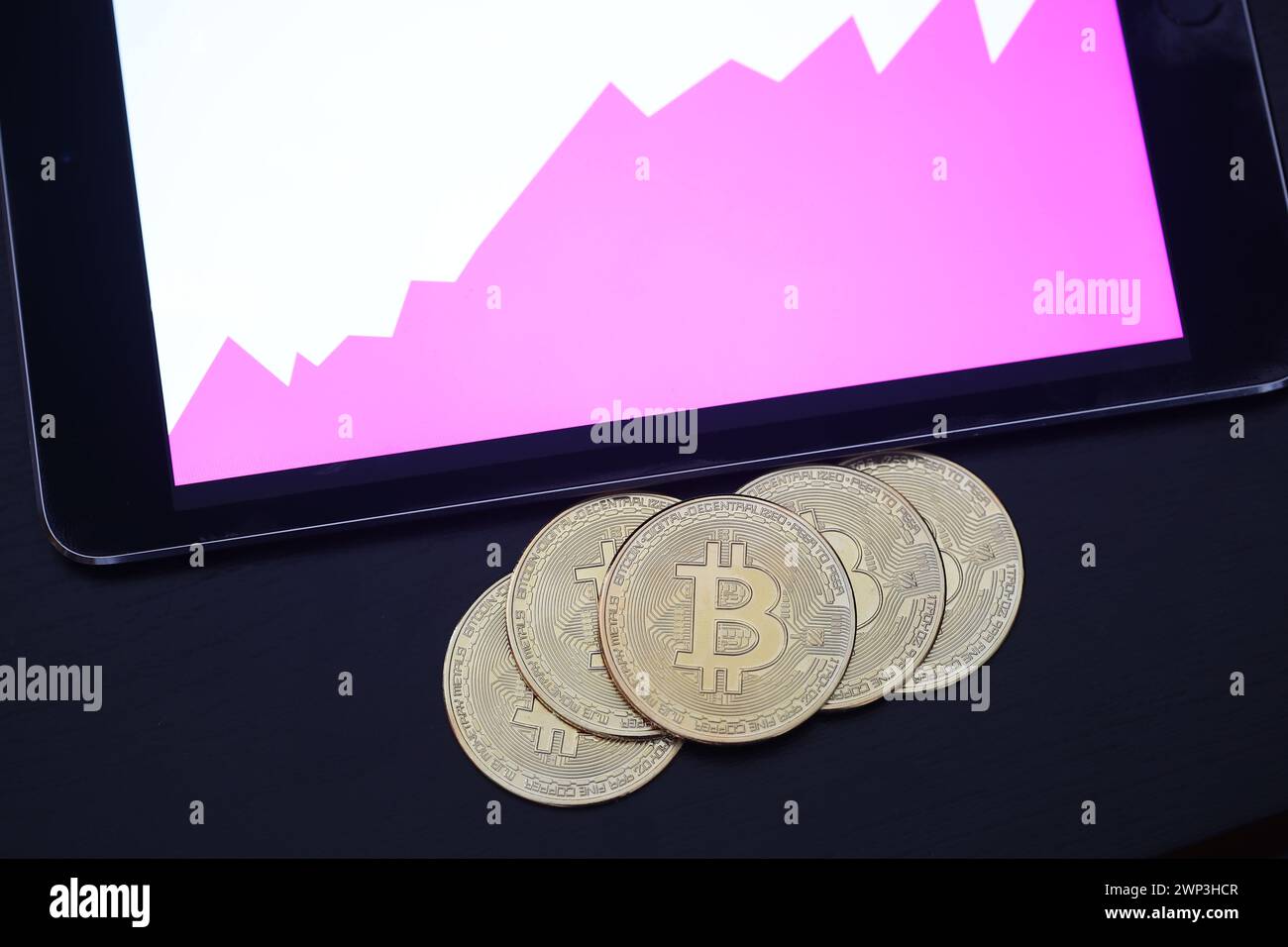 Symbolbild:  Bitcoins vor einem Tablet mit Finanzdaten - Der Bitcoin steht hoch im Kurs. Selbst Finanzdienstleister wie Paypal wollen die Kryptowährun Stock Photo