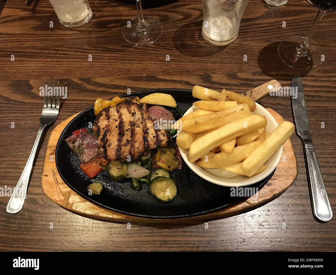 Grilled chicken and fries with veg, courgettes on a plate and drinks at a local restaurant Stock Photo