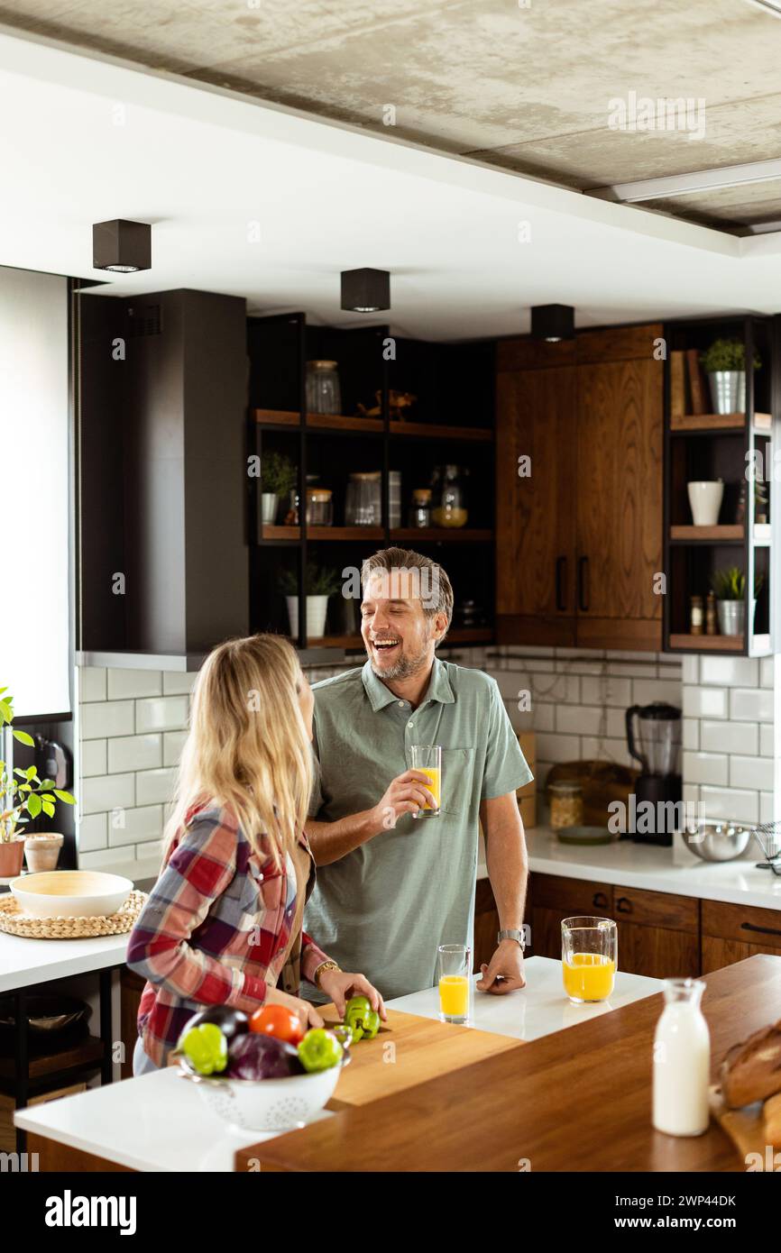 A pair enjoying a lighthearted conversation with fresh juice and a healthy breakfast spread on the counter. Stock Photo