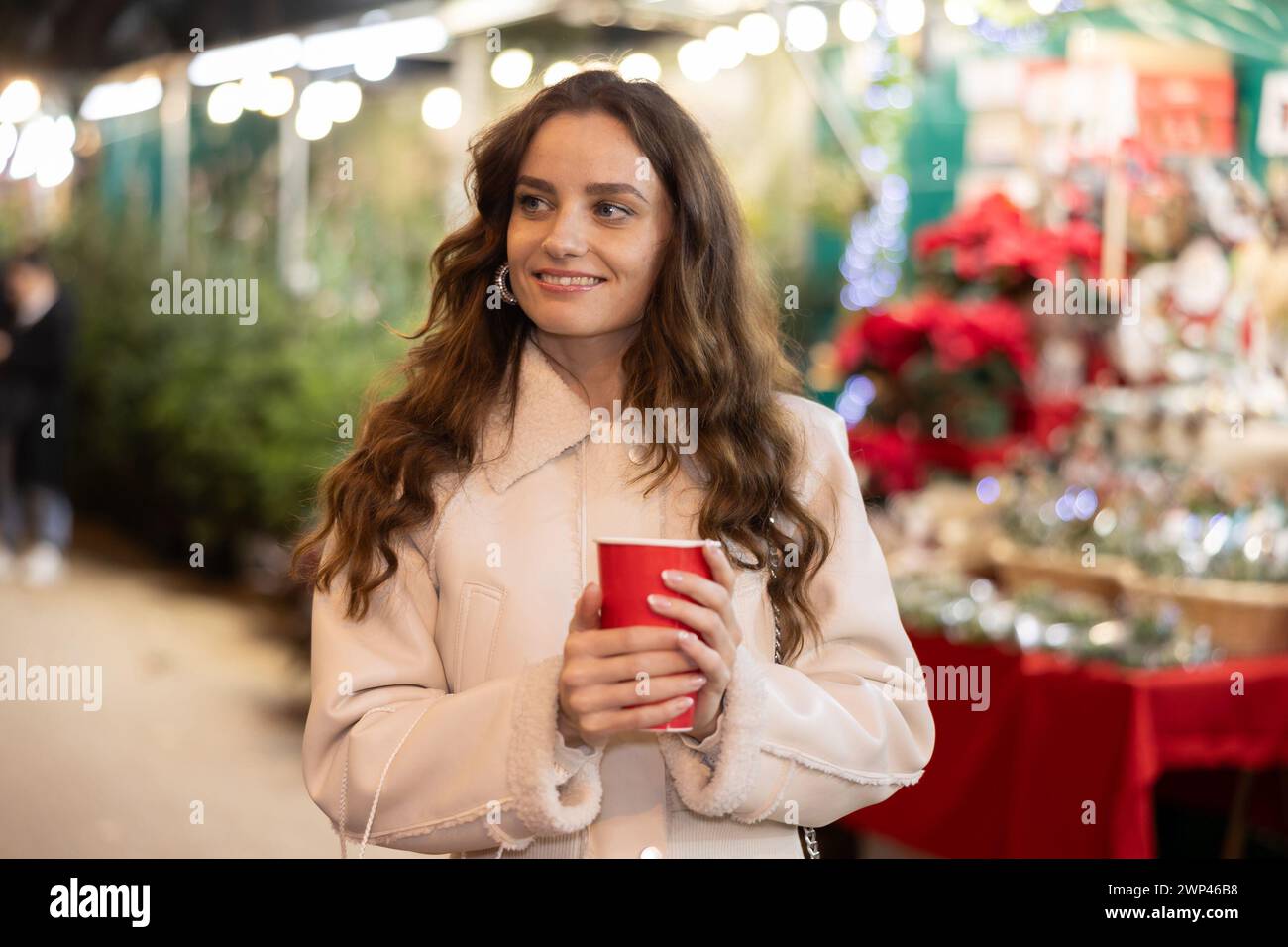 Smiling woman walking through Christmas street market with warm beverage in paper cup Stock Photo